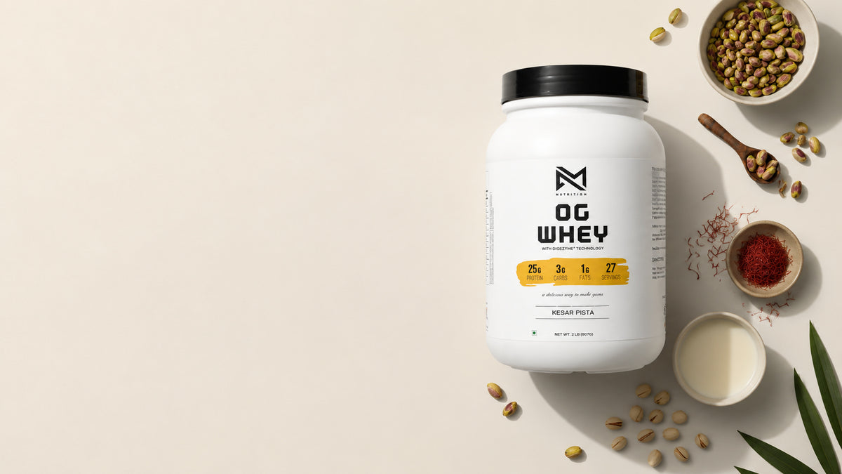 A white tub of OG Whey protein powder with a black lid and yellow label accents, styled in a flat-lay with scattered soybeans, a bowl of milk, and small bowls of spices on a light beige background.